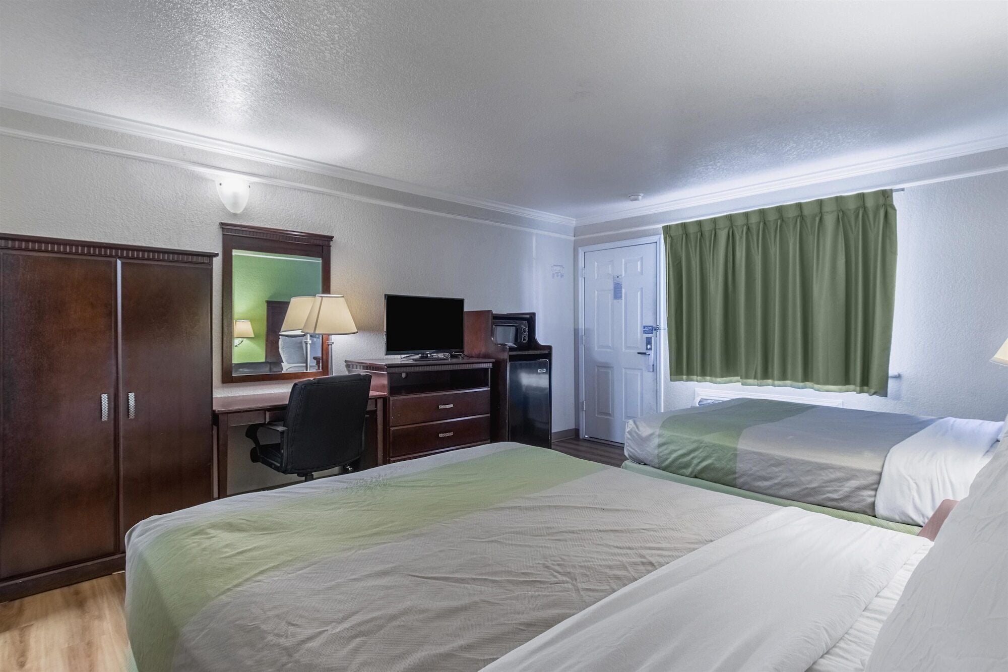 A hotel room with two beds, a desk with a computer, a TV, and a minibar.