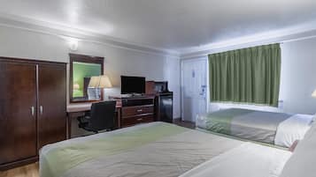A hotel room with two beds, a desk with a computer, a TV, and a minibar.