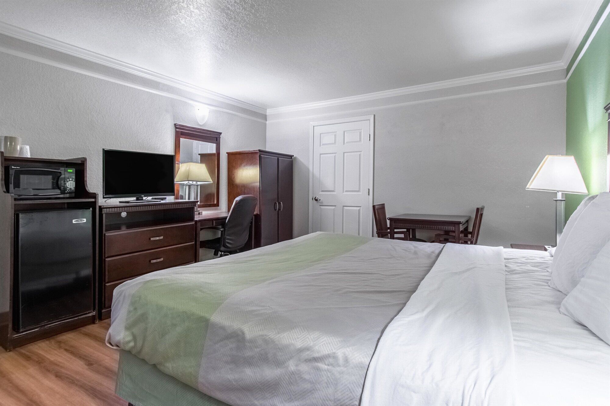 Een hotelkamer met een bed, een bureau met een computer, een stoel, een magnetron, een koelkast en een deur.