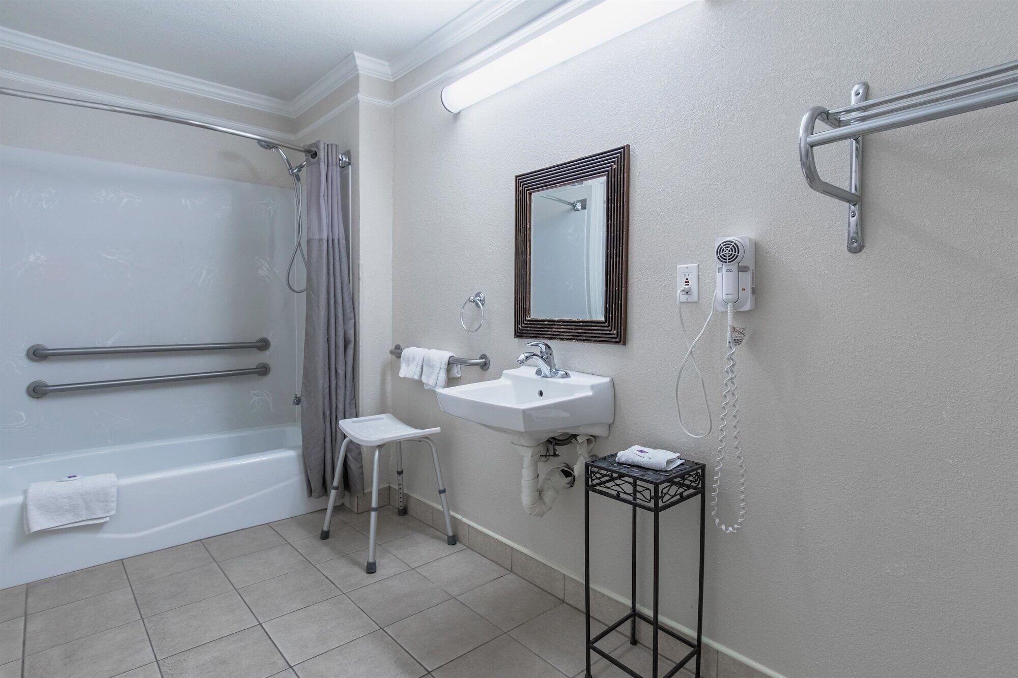 A bathroom with a bathtub, a sink, a mirror, and a shower with grab bars.