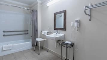 A bathroom with a bathtub, a sink, a mirror, and a shower with grab bars.