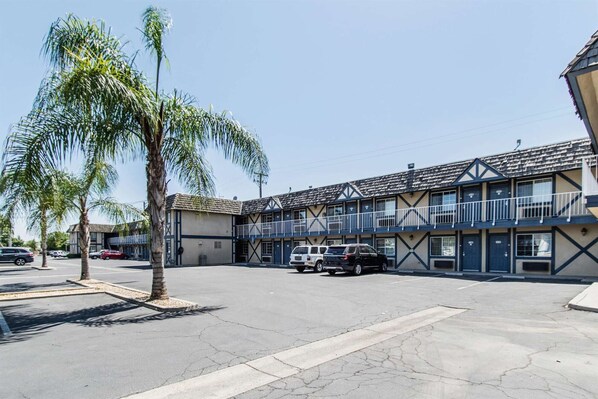 Un motel con una estructura de dos pisos, un estacionamiento y una palmera.