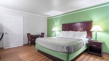 A hotel room with a green wall, a wooden floor, a bed with white bedding, a wooden headboard, two bedside tables with lamps, and a desk with a chair.