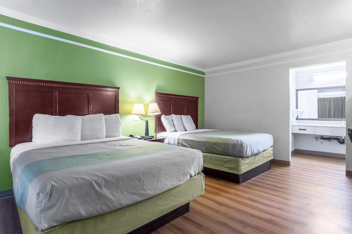 Una habitación de hotel con dos camas, una pared de acento verde, suelo de madera y una ventana con cortinas.