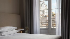 A hotel room with a bed, a small table, and a window with a view of a building. - Palazzo Firenze by Baglioni Hotels & Resorts (Florence)