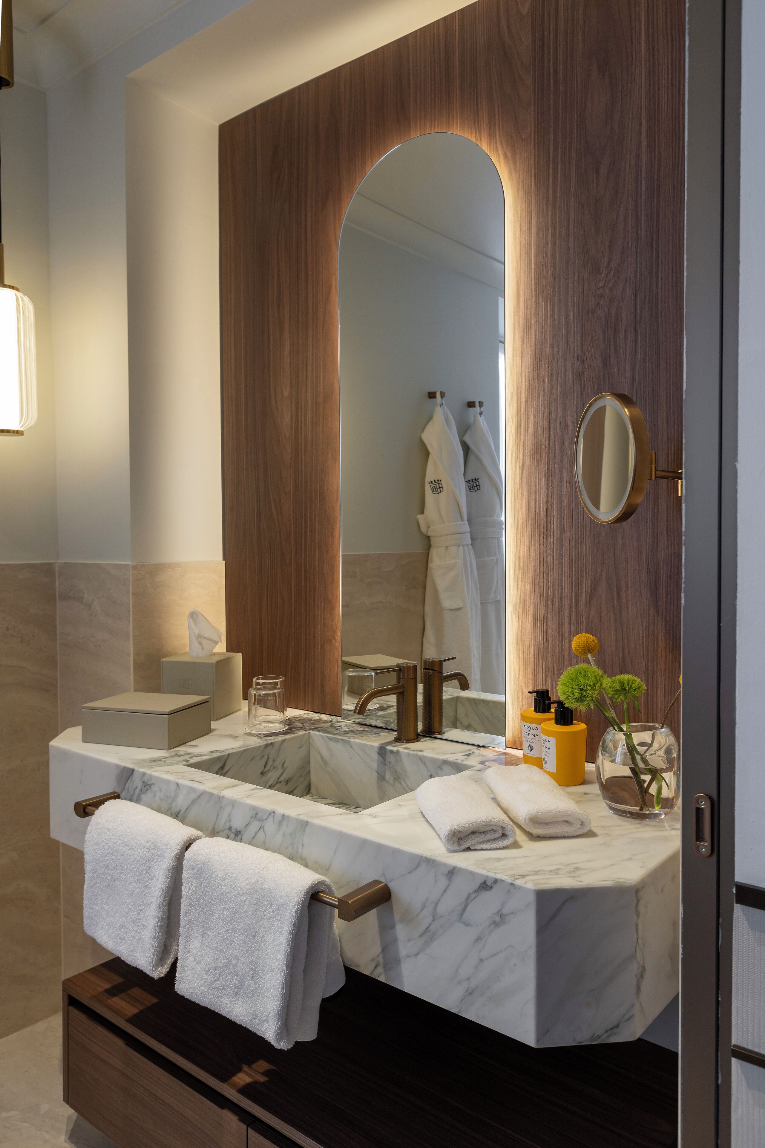 Un baño con lavamanos de mármol, paneles de madera, un espejo grande y toallas.