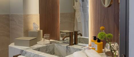 Un baño con lavamanos de mármol, paneles de madera, un espejo grande y toallas.