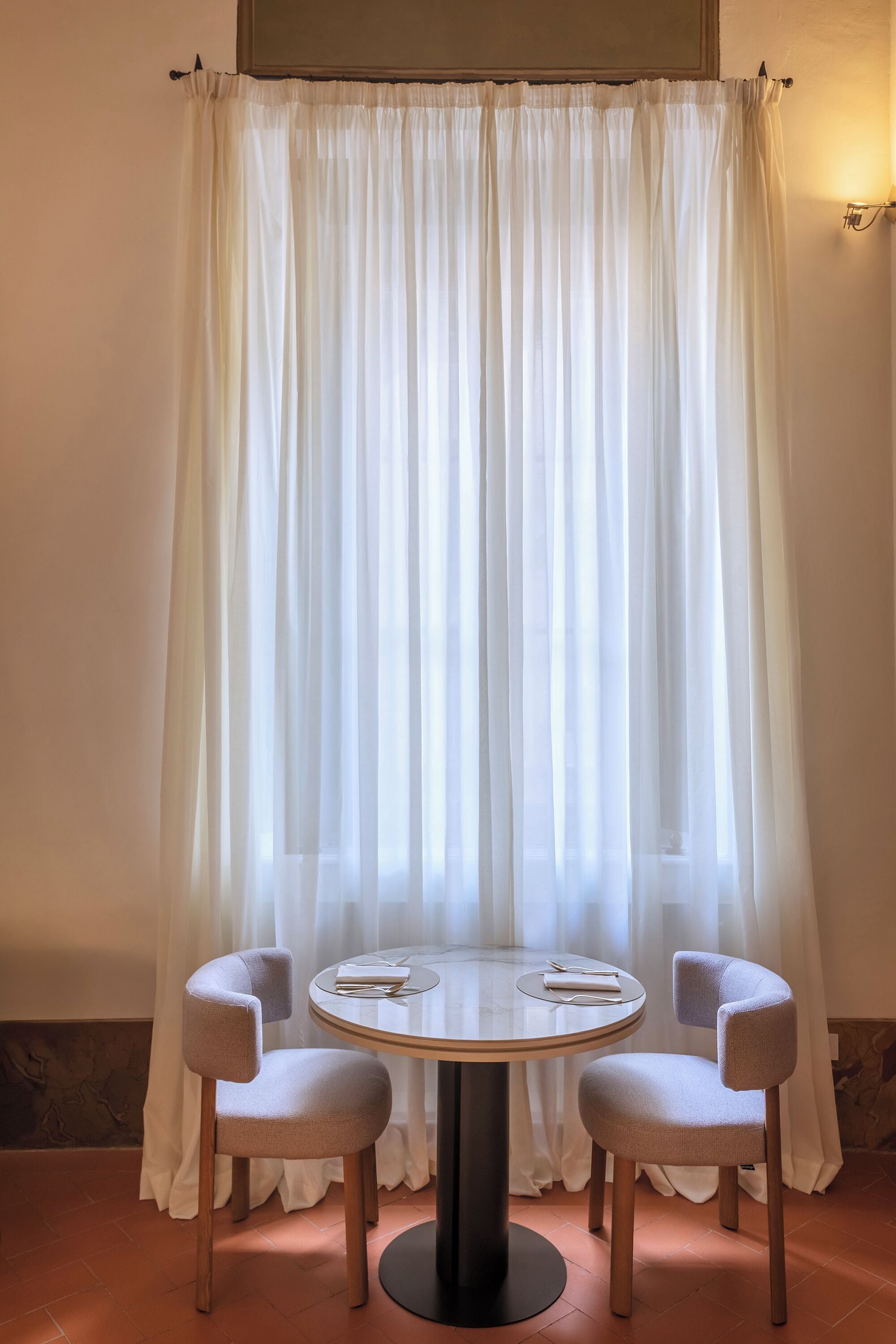 A room with a round table, two chairs, and a curtain.