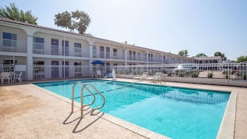 Un área de piscina con una piscina azul cristalina, sillas blancas junto a la piscina y un edificio con balcones.