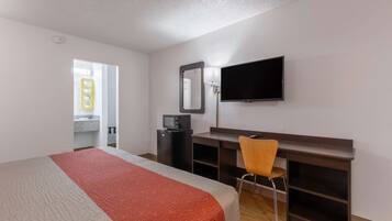 A hotel room with a bed, a desk, a chair, a TV, and a mirror.