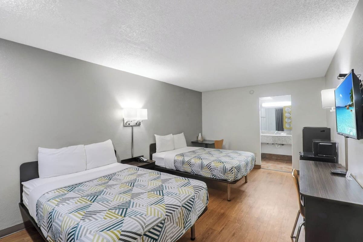 A hotel room with two beds, a desk, a TV, and a bathroom mirror.