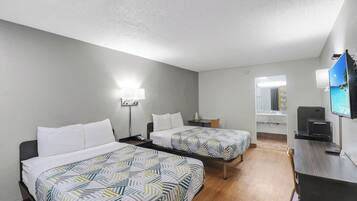 A hotel room with two beds, a desk, a TV, and a bathroom mirror.