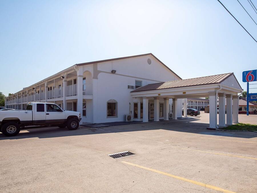 A two-story motel with a covered parking area and a white pickup truck parked in front.