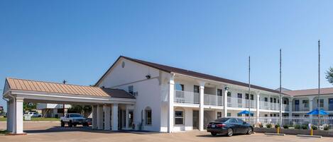 Un motel à deux étages doté d’un parking couvert, d’une annexe d’un seul étage et surplombant un ciel d’un bleu limpide.