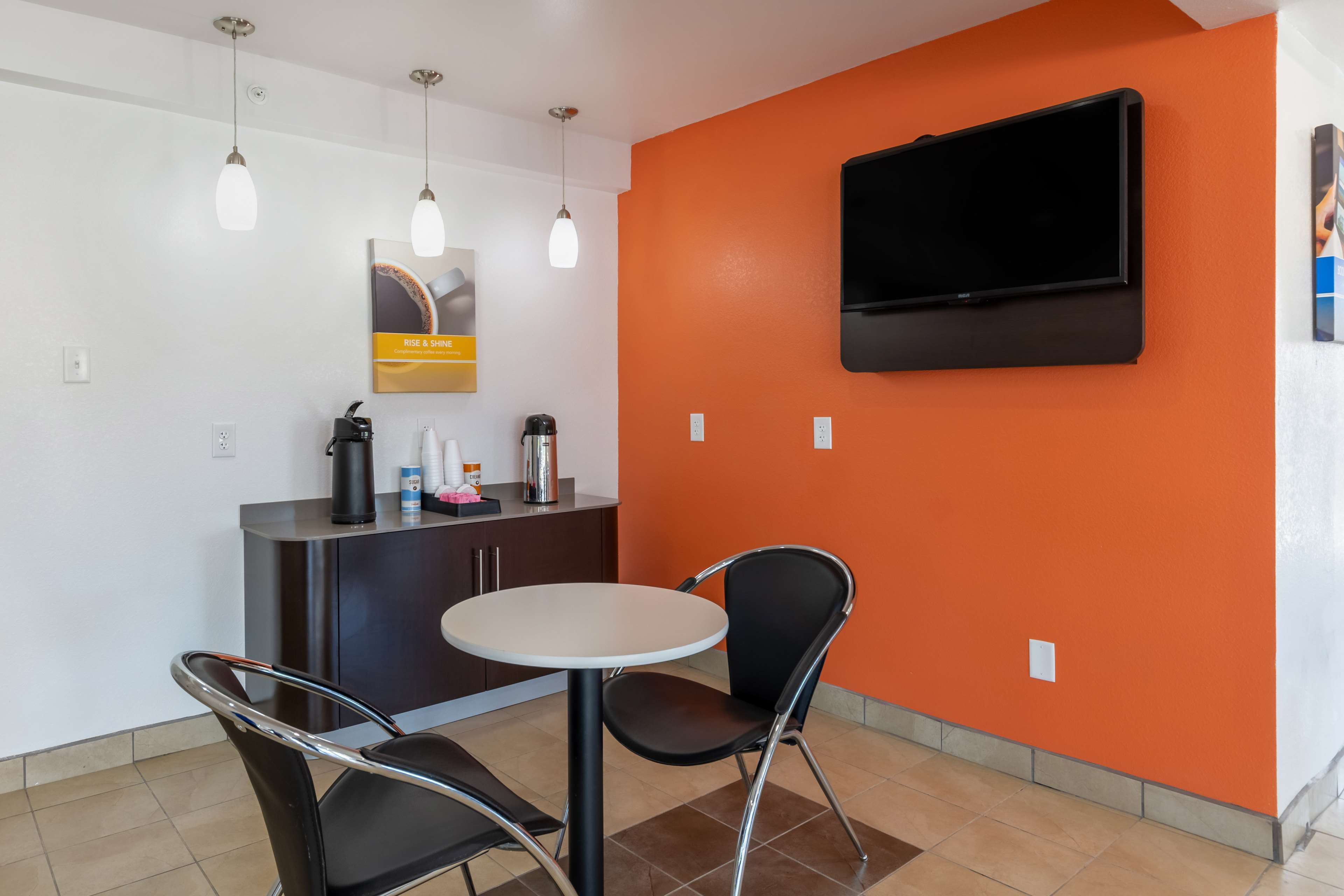 Een hotelkamer met een receptiebalie, een televisie aan de oranje muur, een ronde tafel en twee stoelen.