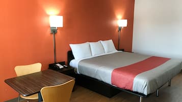 Una habitación de hotel con cama, escritorio, dos sillas y dos lámparas de noche.