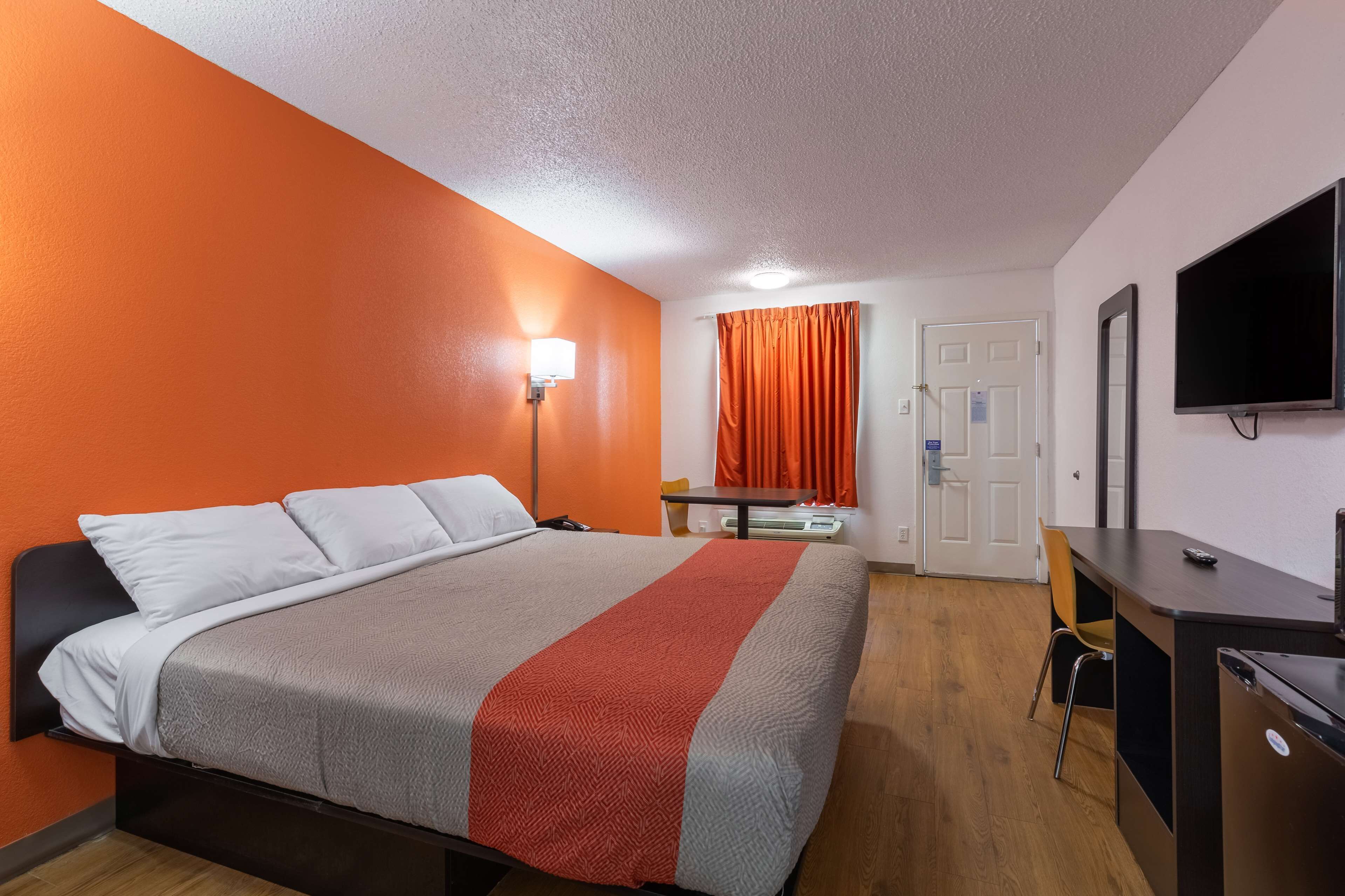 A hotel room with a bed, a desk, a chair, a television, and a door.