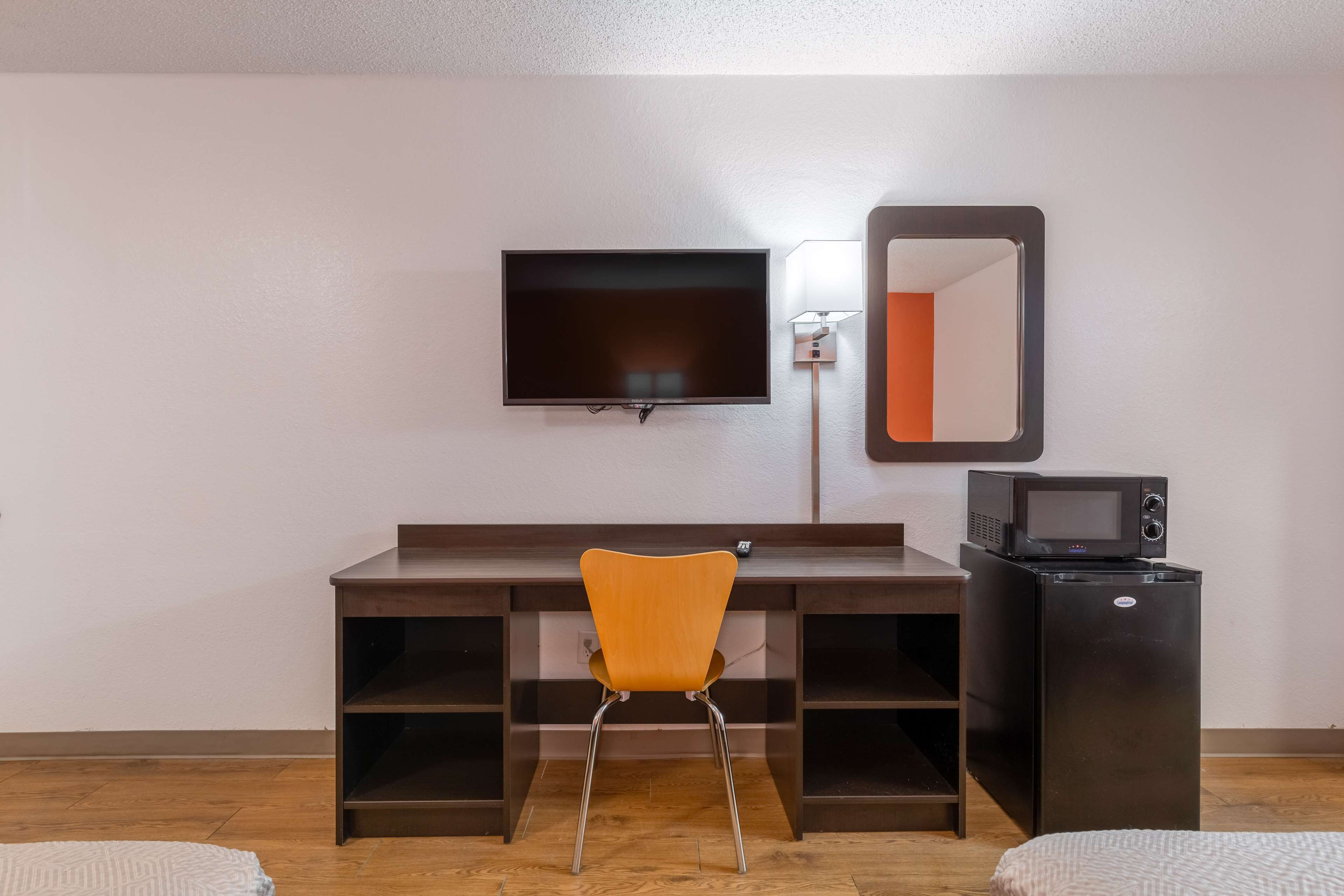 A room with a wooden desk, a television mounted on the wall, a microwave, and a chair.