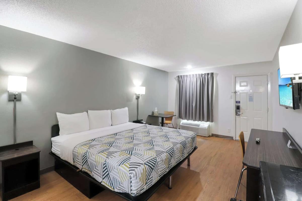 A hotel room with a bed, bedside lamps, a desk, a chair, a TV, and a window with curtains.