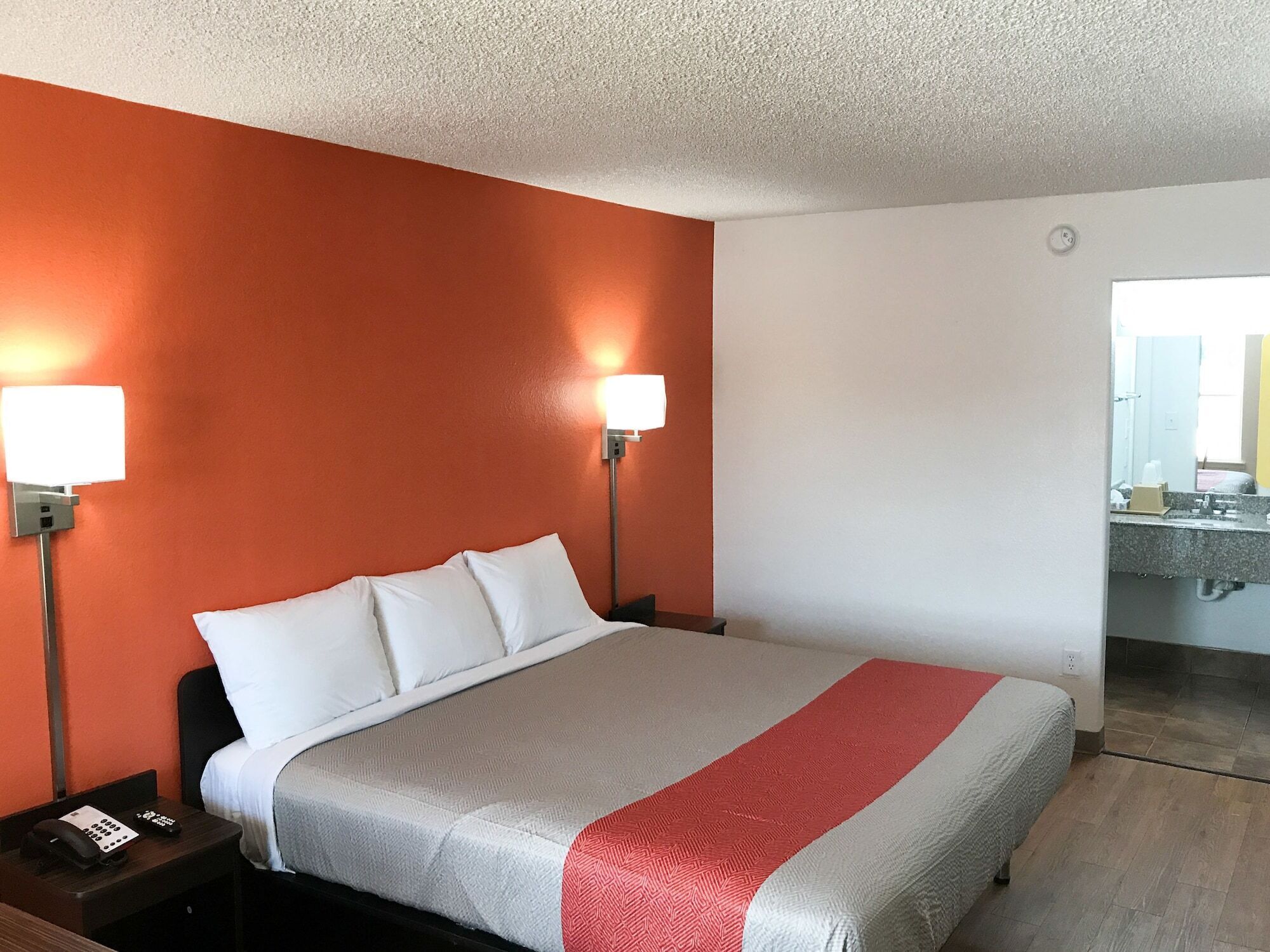 Habitación de hotel con cama, dos lámparas de noche, una mesita con teléfono, y baño visible a través de una puerta abierta.