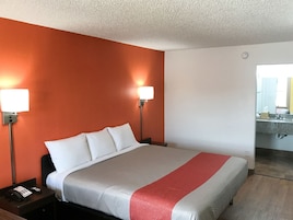 Habitación de hotel con cama, dos lámparas de noche, una mesita con teléfono, y baño visible a través de una puerta abierta.