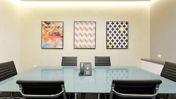 A conference room with a glass table, four black chairs, a telephone, and three framed artworks on the wall.