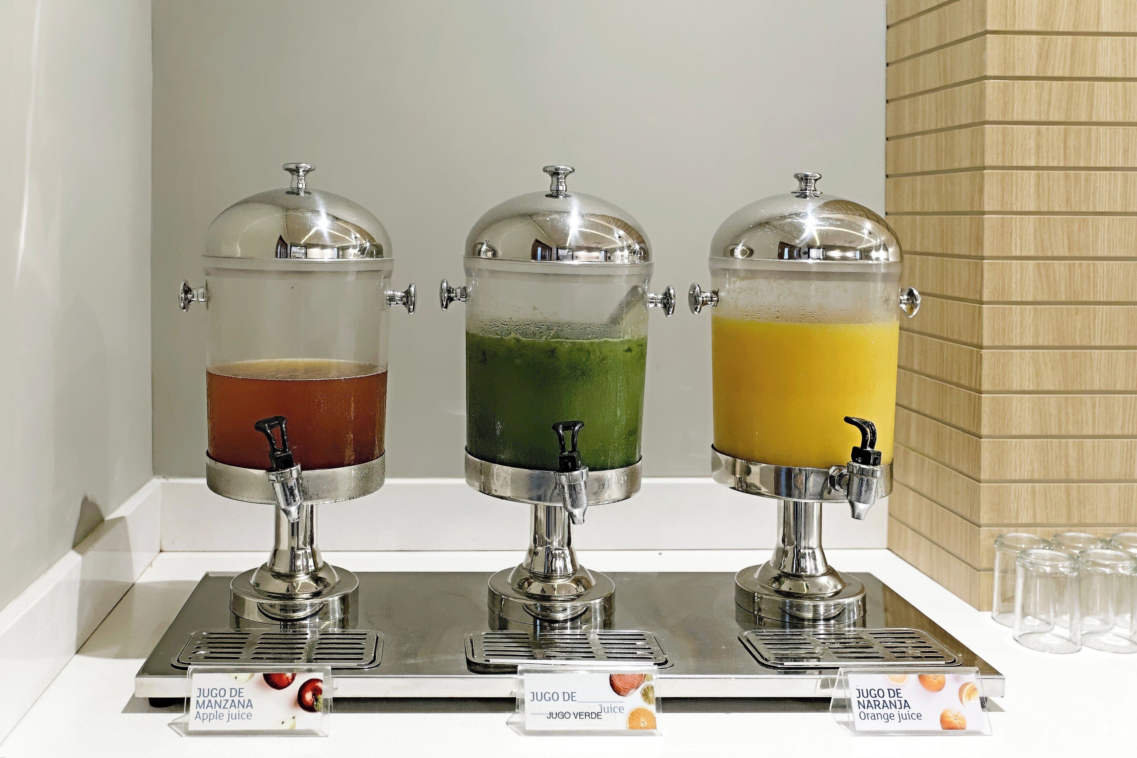 Una estación de bebidas con tres dispensadores, cada uno identificado con un jugo de fruta diferente.