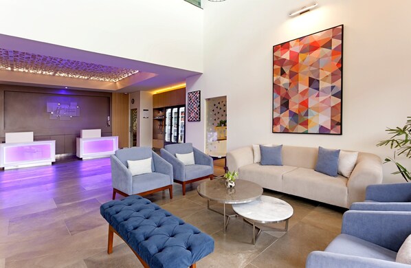 Um saguão de hotel moderno com balcão de recepção, área de estar e uma grande pintura abstrata.