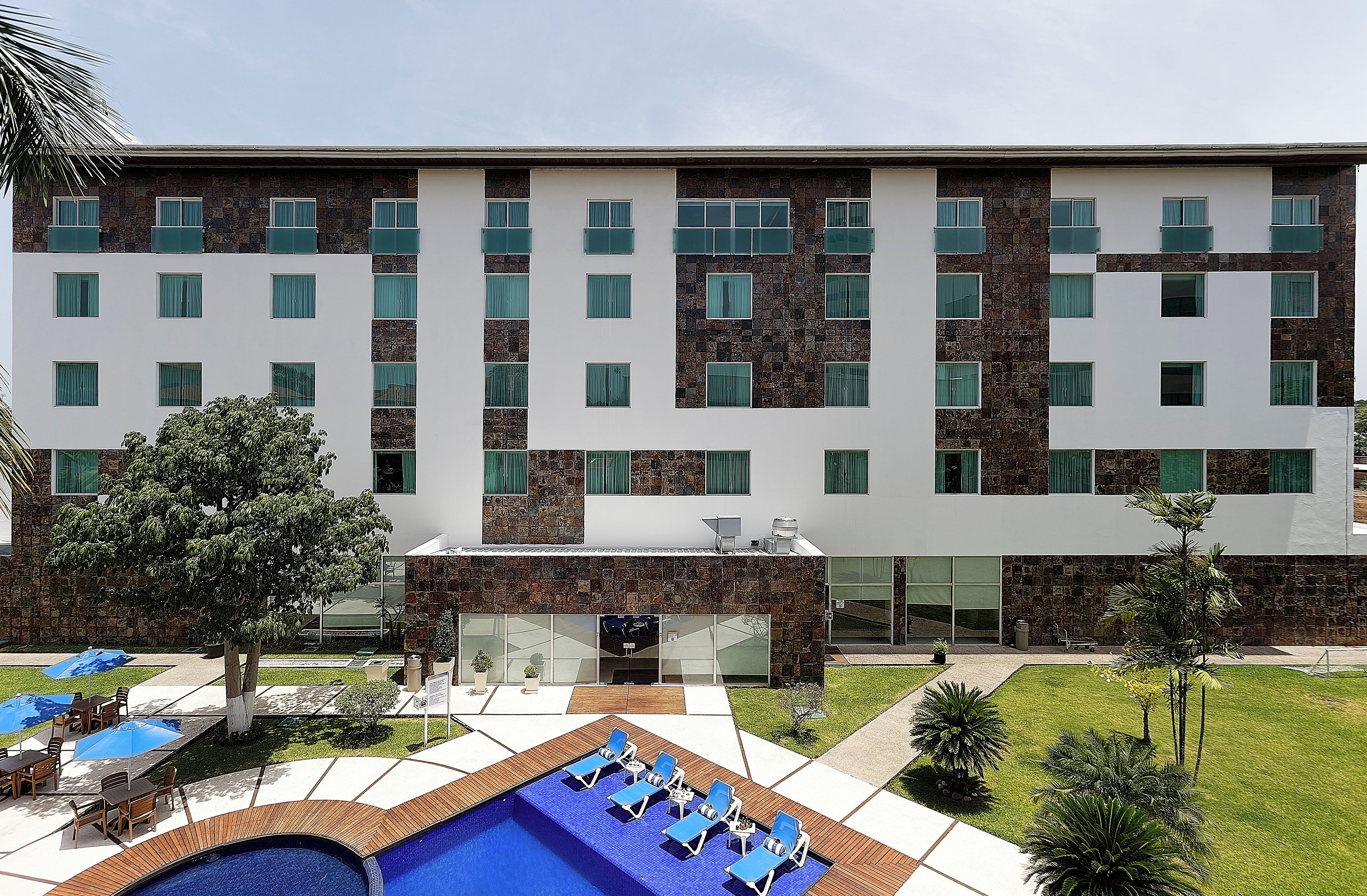 Un hotel moderno con zona de piscina, mobiliario exterior y fachada de piedra y blanco.