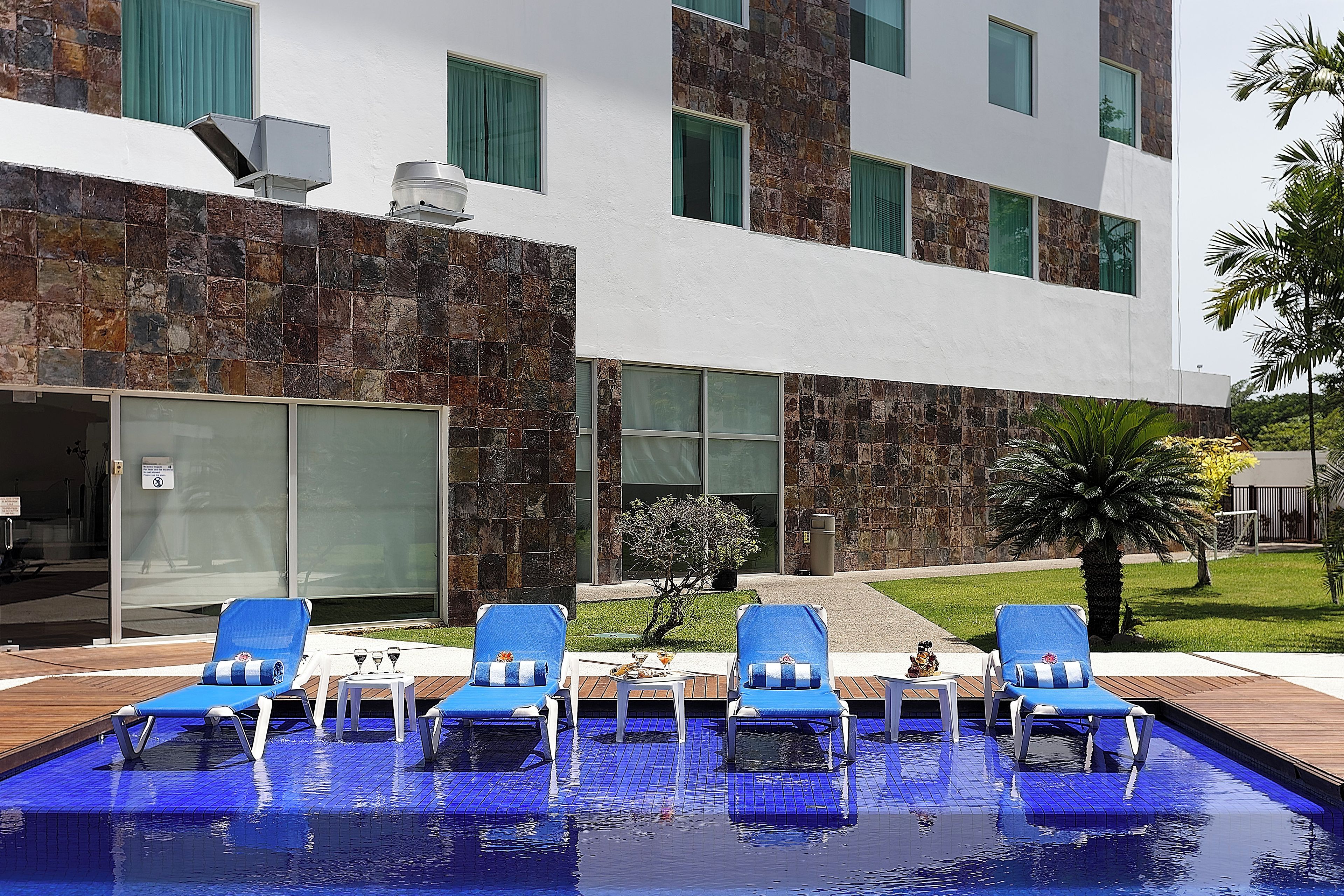 Un área de piscina con sillones de descanso y un edificio de fachada de piedra y ventanas amplias.