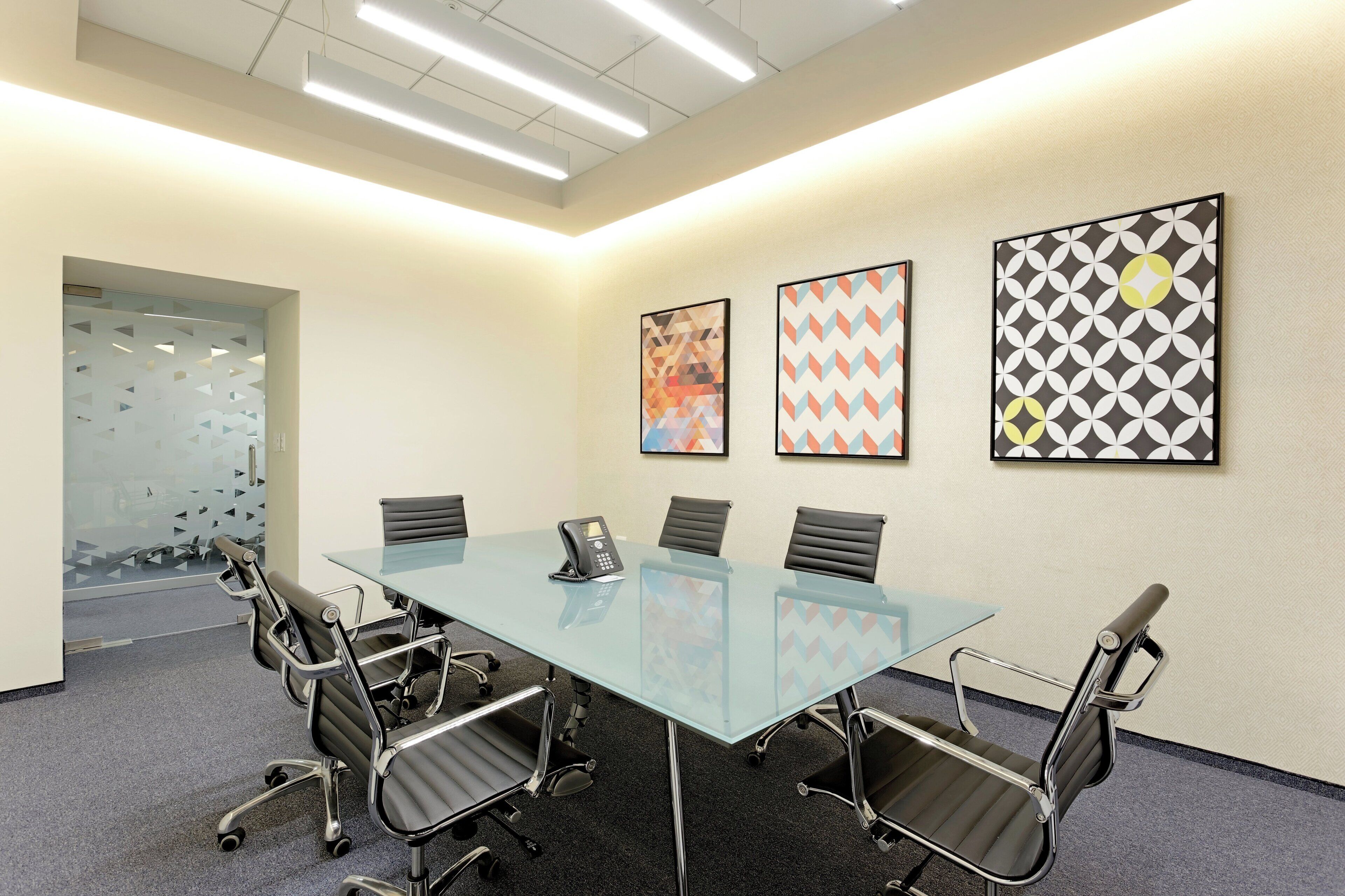 A conference room with a glass table, six chairs, and three framed artworks on the wall.