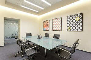A conference room with a glass table, six chairs, and three framed artworks on the wall.