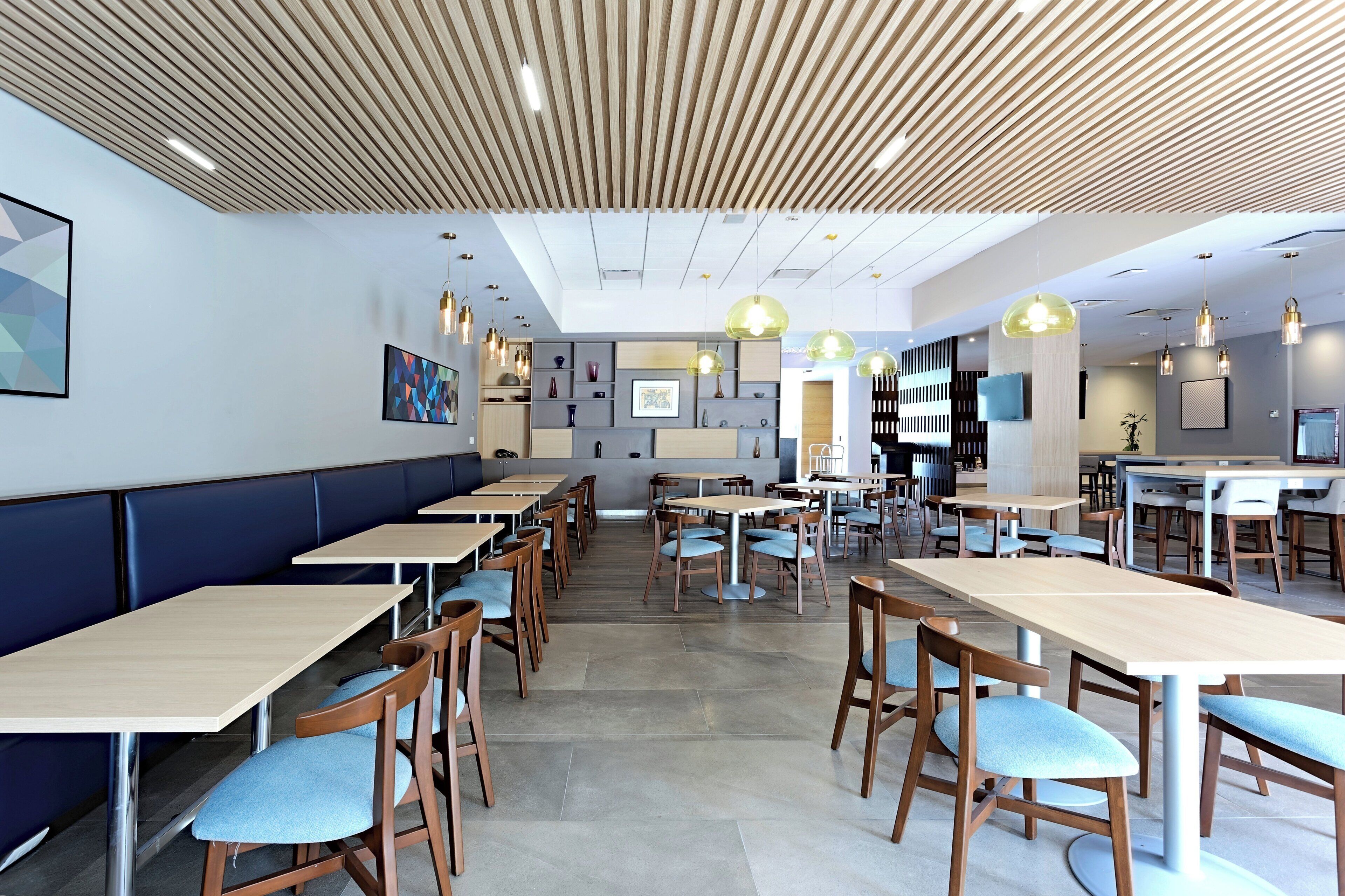 Un interior de restaurante moderno con mesas de madera, sillas con cojines azules e iluminación colgante.