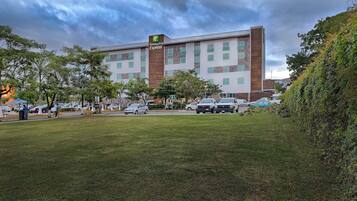 Un bâtiment de la chaîne Holiday Inn Express, doté d’un design moderne, avec une façade combinant brique et pierre, de nombreuses fenêtres et un parking où sont stationnées plusieurs voitures.
