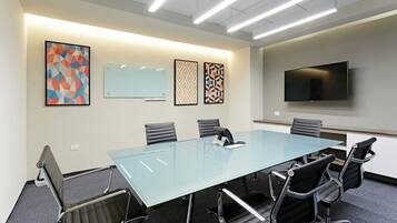 A conference room with a glass table, six chairs, a whiteboard, and a flat-screen TV on the wall.