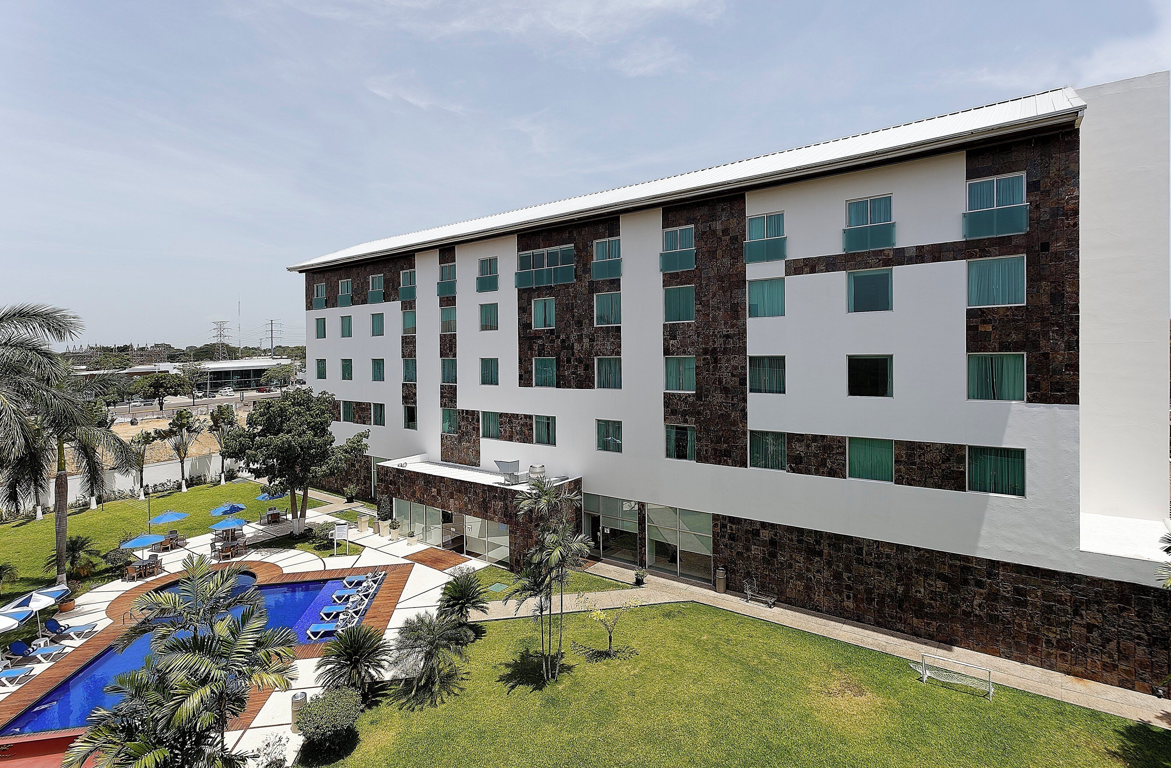 A multi-story hotel with a pool area, outdoor seating, and a well-maintained lawn.