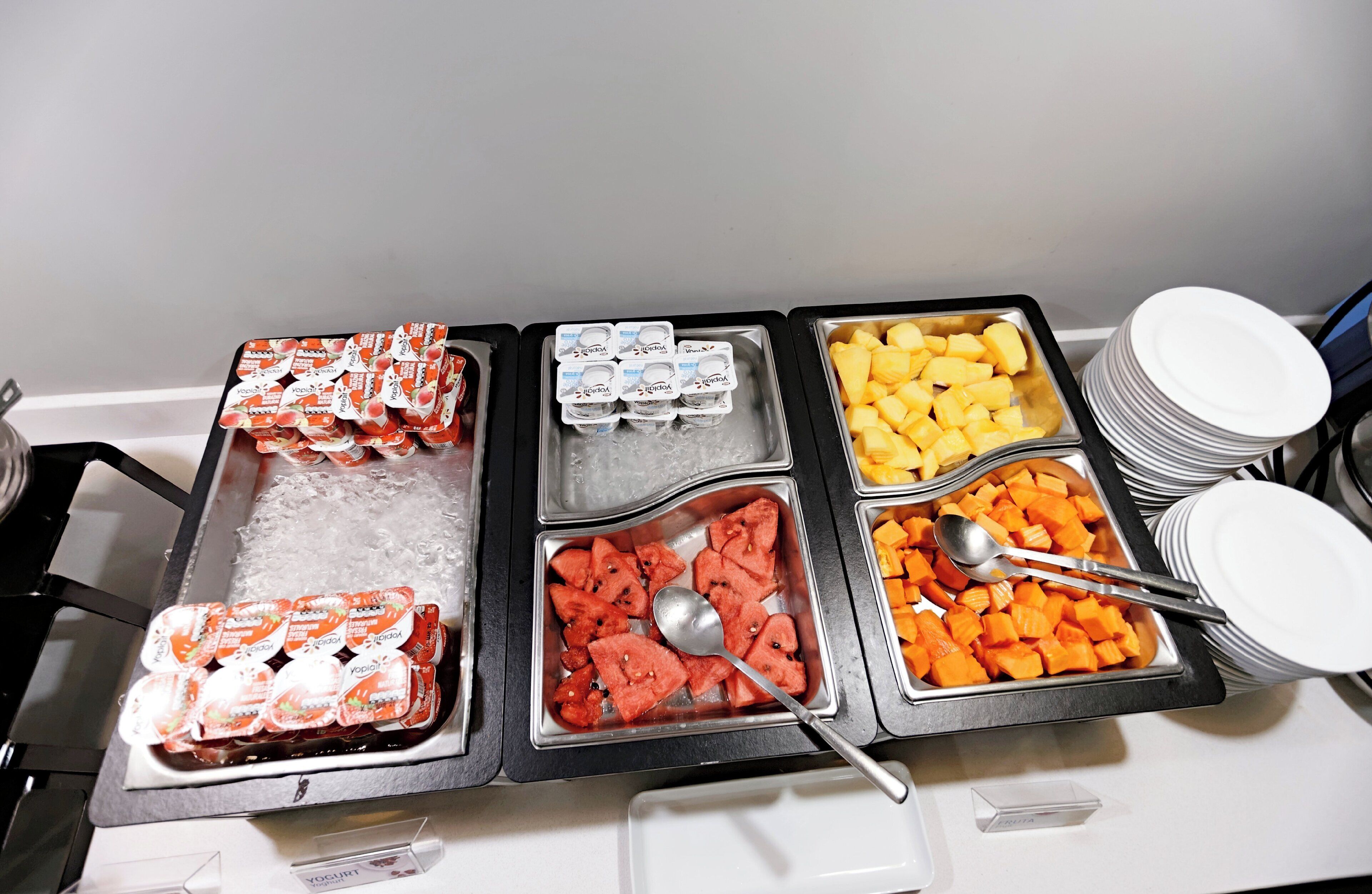 A buffet with various food items including yogurt, watermelon, pineapple, and carrots.