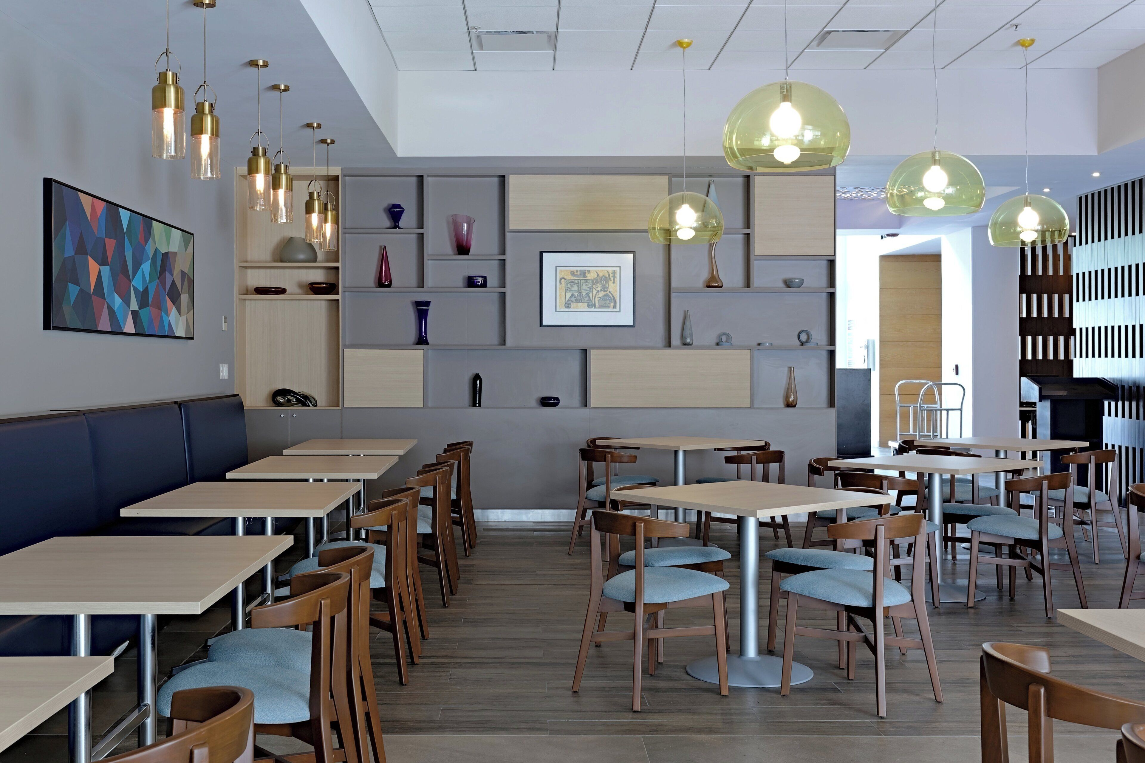 Un interior de restaurante moderno con múltiples mesas y sillas, iluminación colgante y estantes decorativos en la pared.