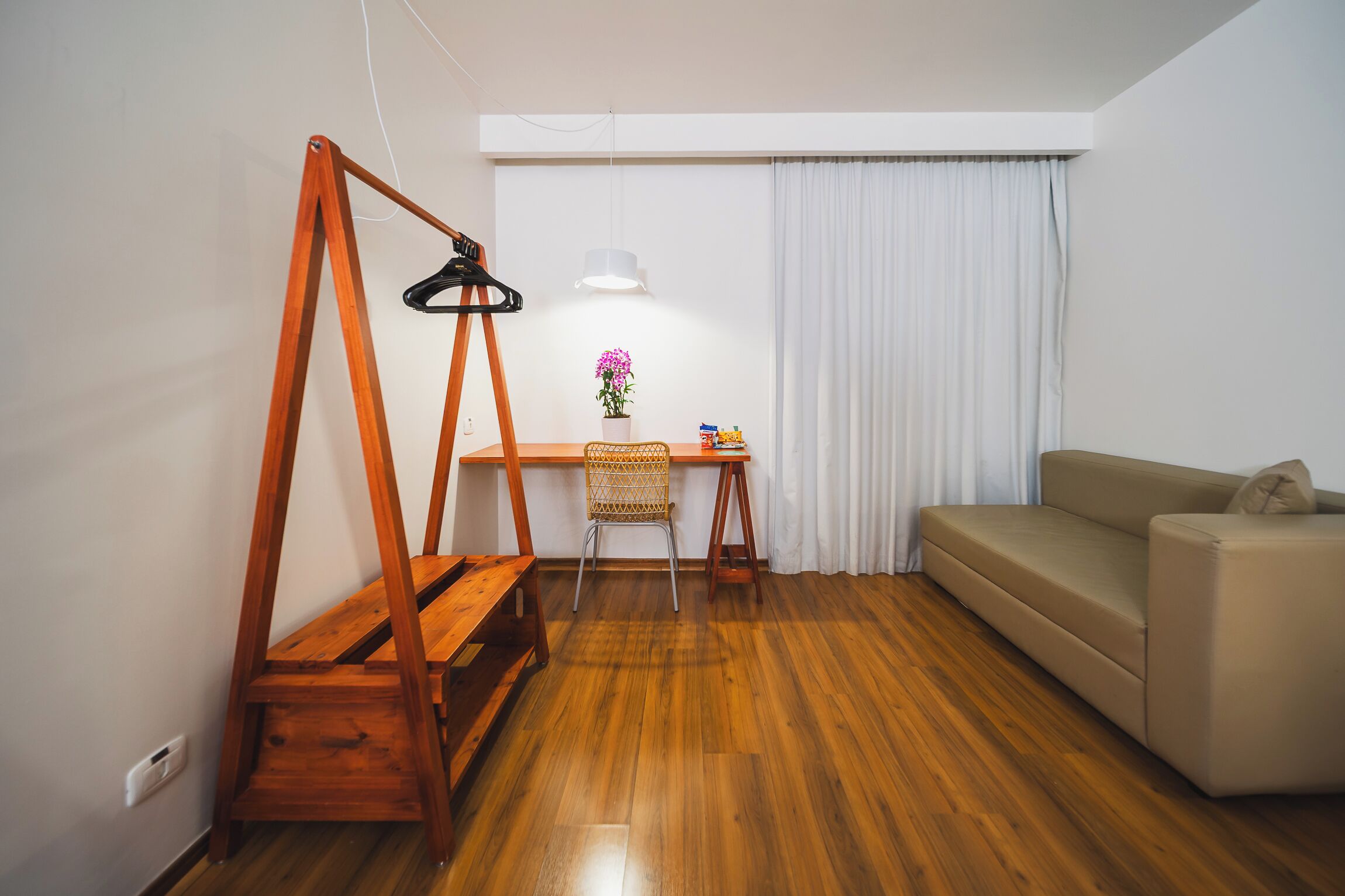 A room with a wooden desk, a chair, a sofa, and a hanging light fixture.