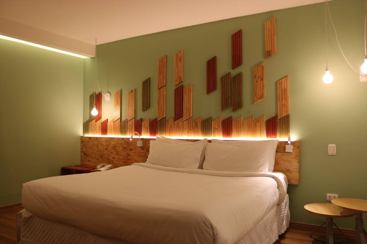 Een slaapkamer met een groot bed, een houten hoofdbord, een nachtkastje en een klein rond tafeltje.