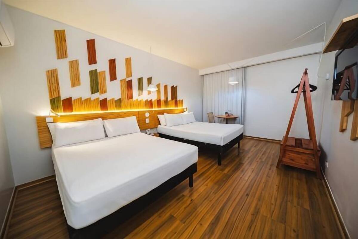 Een hotelkamer met twee bedden, een houten vloer, een kunstinstallatie aan de muur en een kapstok.