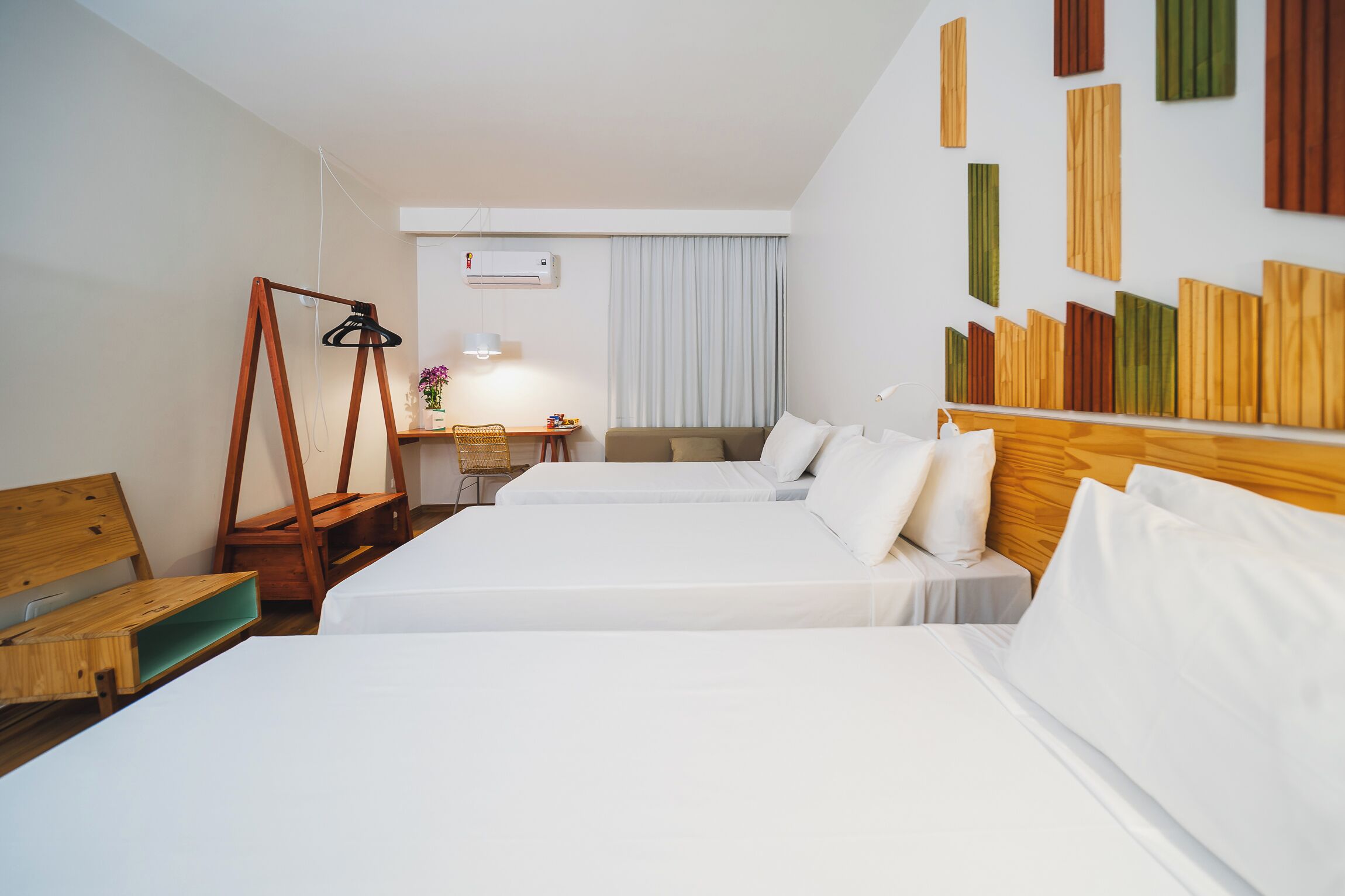 Une chambre d’hôtel avec deux lits, une tête de lit en bois, un bureau avec une chaise et un climatiseur fixé au mur.