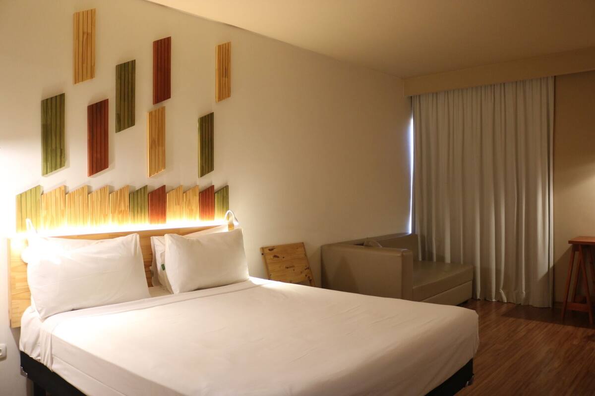 Een hotelkamer met een groot bed, een houten hoofdeinde, een bank en een raam met gordijnen.