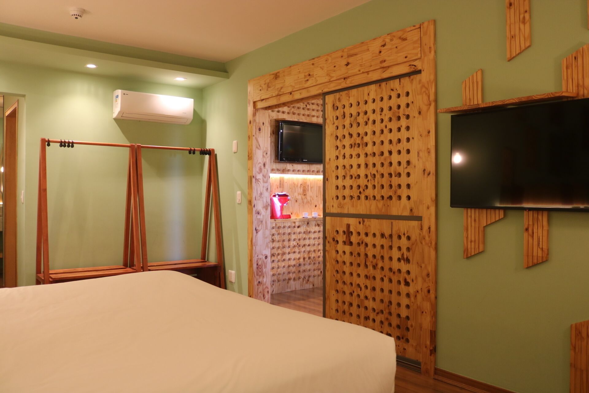 A hotel room with a bed, a TV mounted on the wall, a wooden wardrobe, and a shower area.