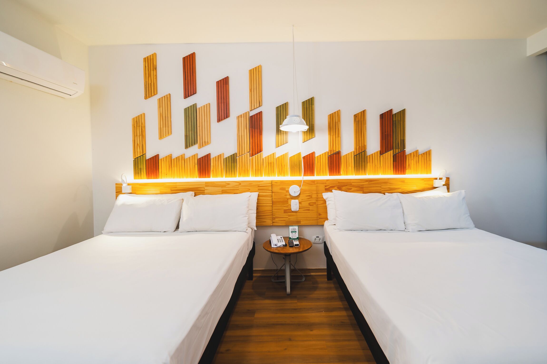 A hotel room with two beds, a wooden headboard, a small table with a phone, and a wall-mounted light fixture.