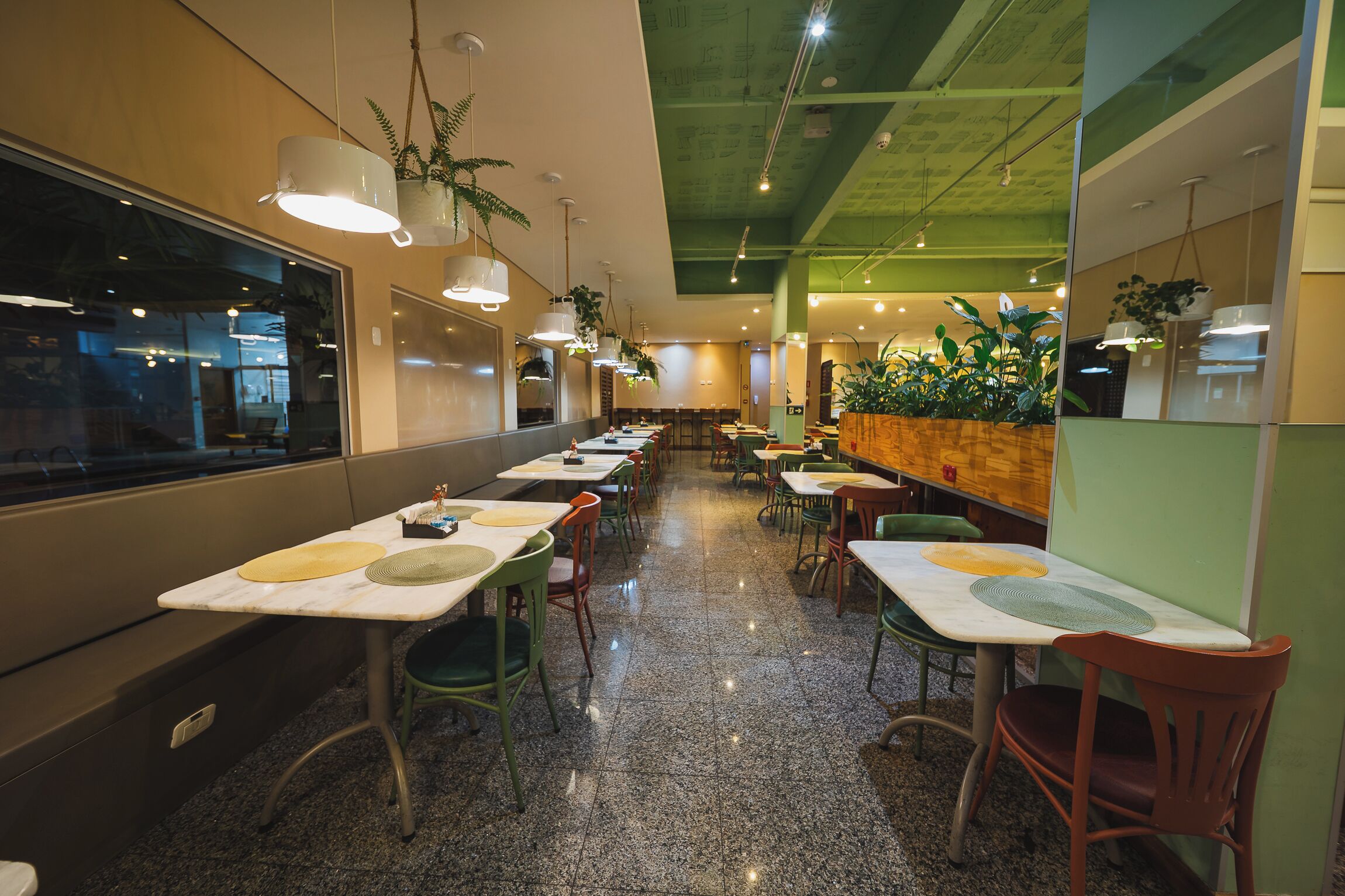 Um restaurante com várias mesas e cadeiras, teto verde e plantas pendentes.