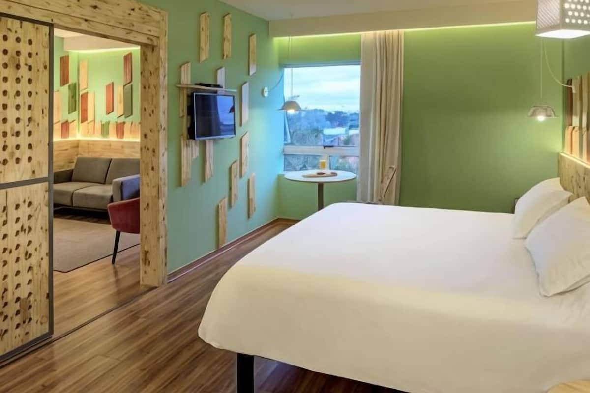 Een hotelkamer met een bed, een televisie, een klein tafeltje en uitzicht op het omliggende landschap.