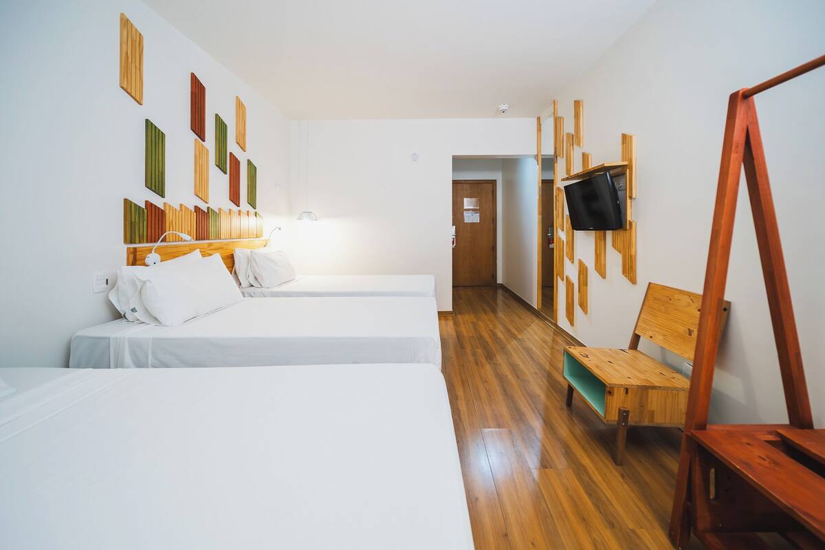 Een hotelkamer met twee bedden, een aan de muur bevestigde televisie, houten vloeren en een houten bankje.
