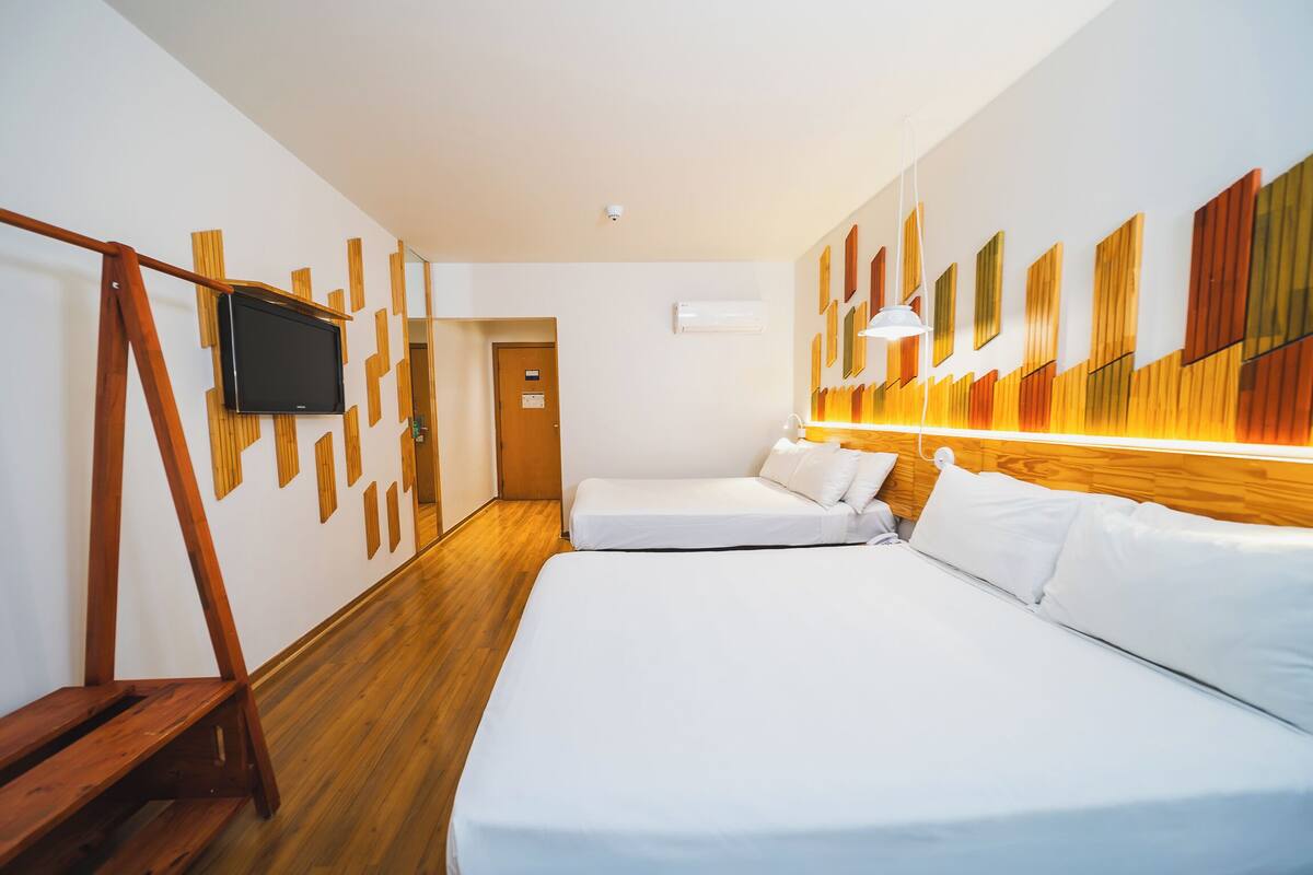 Hotelkamer met twee bedden, een televisie bevestigd aan een houten wandpaneel, een houten vloer en een wandlamp.
