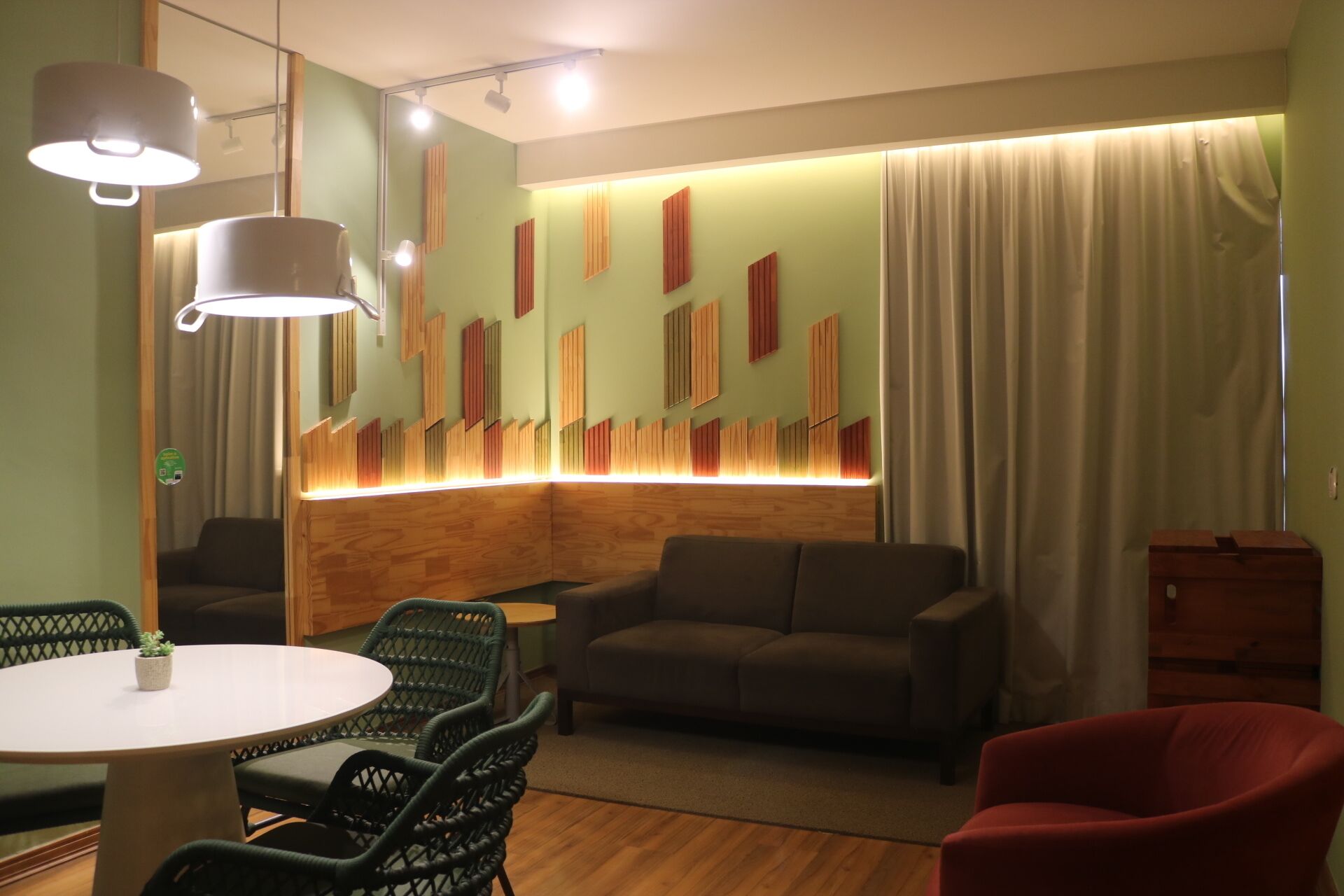 Una sala de estar moderna con una pared de acento de madera, una mesa de comedor redonda con sillas, un sofá y un sillón rojo.